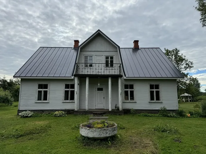 Vana puitelamu uue tumehalli valtsplekk-katusega, kaks punast korstnat